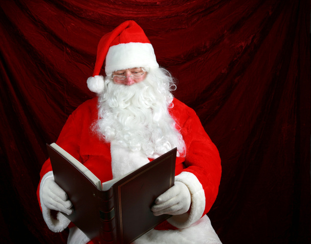 いたずらかニース。サンタクロースは、今年のクリスマス前にいたずらやニースされている彼の大きな本から読みます。サンタクロースはいたずらと素敵な本を持っています。サンタクロースはいたずらやニースされている人に注意を払っています。サンタはいいと言ってる.  - 写真・画像