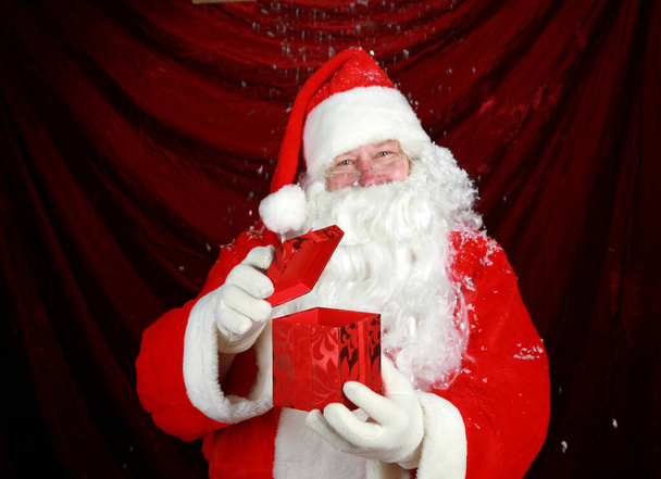 Santa Claus Navidad. Santa Claus está emocionado por lo que ve en un regalo de Navidad de terciopelo rojo dado a él por sus elfos como un regalo de Navidad para él. Santa Claus tiene un regalo de Navidad para ti. Papá Noel en su traje tradicional de terciopelo rojo.  - Foto, imagen