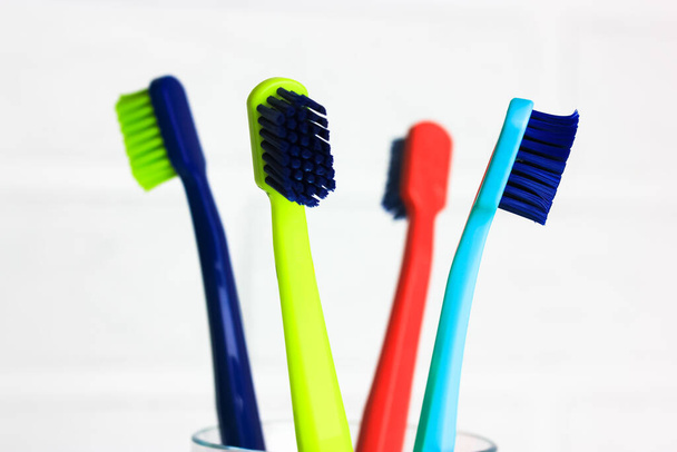 プラスチック製の多色歯ブラシのセット-緑、青、赤、紫-白い背景に透明なガラスに。レンガの壁に対して4つの明るいカラフルな柔らかい歯ブラシでカップ。歯科治療.  - 写真・画像