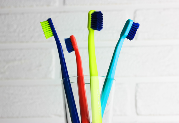 Set van plastic veelkleurige tandenborstels - groen, blauw, rood, paars - in het transparante glas op een witte achtergrond. Beker met vier felgekleurde zachte tandenborstels tegen bakstenen muur. Tandheelkundige verzorging.  - Foto, afbeelding