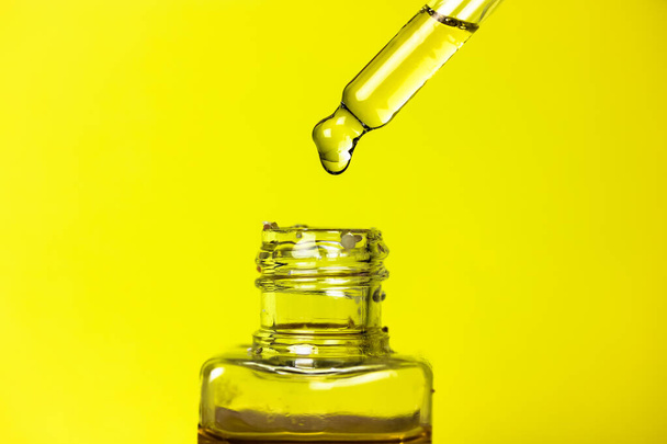 A drop of tanning oil on the tip of the dropper on warm yellow background. Transparent glass botle with a suntan oil to protect the skin of the face and body on hot summer days. Face Care Serum.  - Photo, Image