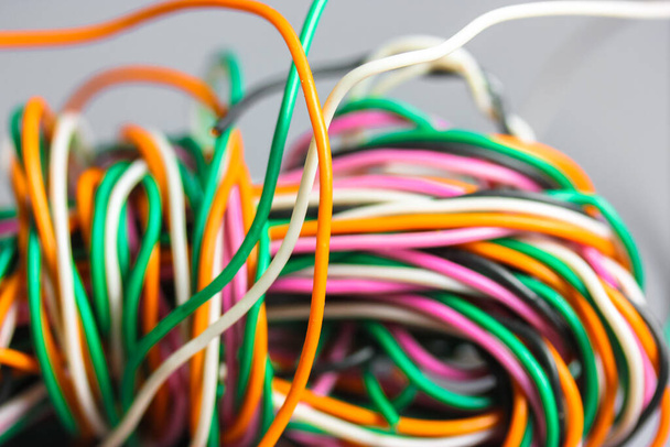 多色の電気、車、コンピュータ、電話線の束を一緒に背景ツイスト。オレンジ、緑、ピンク、グレーの背景に白いケーブル。コンピュータネットワーク、電気通信サービスの概念. - 写真・画像