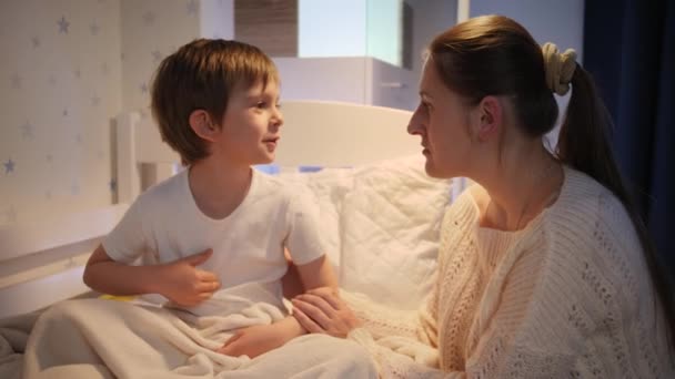 Young loving mother stroking and hugging her little sick son lying in bed at night. Concept of children illness, disease and parent care - Felvétel, videó