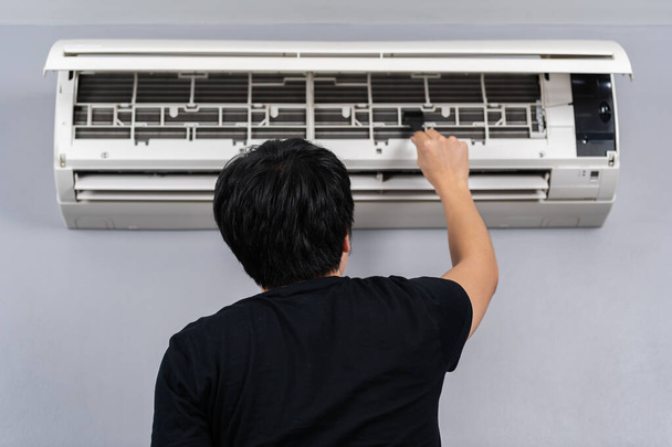 young man using brush to cleaning the air conditioner indoors at hone - 写真・画像