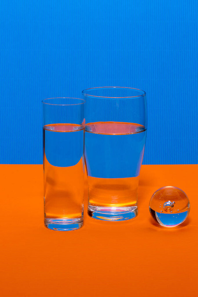 Натюрморт со стеклянными стаканами с жидкостью на цветном фоне - Фото, изображение
