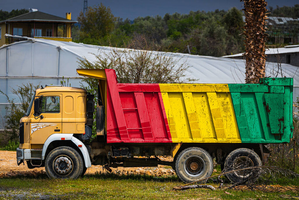Camión volquete con la imagen de la bandera nacional de Guinea está estacionado en el fondo del campo. El concepto de exportación-importación, transporte, entrega nacional de mercancías - Foto, imagen