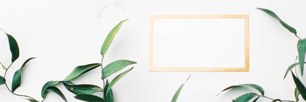 Tarjeta blanca y dorada en blanco, hojas verdes sobre fondo blanco como plano de marco botánico, invitación de boda y marca, diseño de laicos planos - Foto, imagen