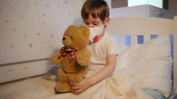 A kisfiú rosszul érzi magát orvosi lélegeztető maszkban és plüssmacival játszik. A gyermekvírus és a gyermekvédelem koncepciója a Covid-19 világjárvány idején. - Felvétel, videó
