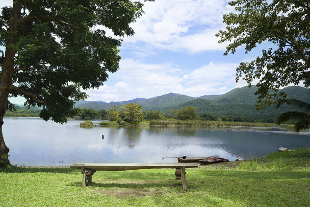 Wooden chairs are placed by the river for outdoor view with blue sky over the mountain and lake view on background. Bench on the lake for Sit and relax in a shady atmosphere amidst nature. - Photo, Image