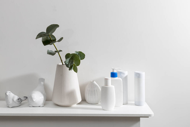 Figurines of a bird are on the surface of the chest of drawers. A vase with a eucalyptus branch, plastic bottles of shampoo, cream. Bathroom. Space for text - Fotoğraf, Görsel