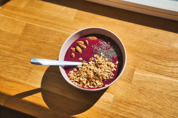 A bowl of morning meal on a wooden windowsill with granola and nuts - Valokuva, kuva