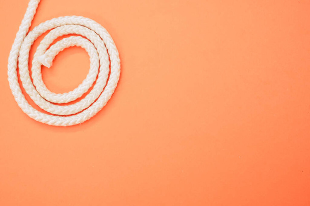 a top view of a white spiral rope on the pastel orange background on the left side - Photo, image