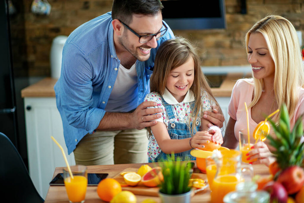 Madre, padre e hija haciendo jugo de naranja fresco en casa en la cocina.  - Foto, Imagen
