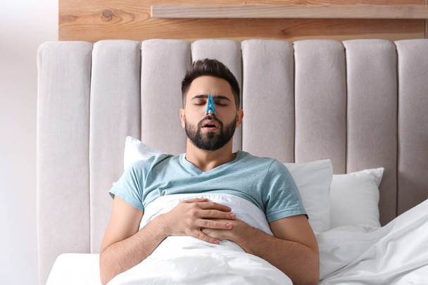Man with clothespin suffering from runny nose in bed - Fotografie, Obrázek