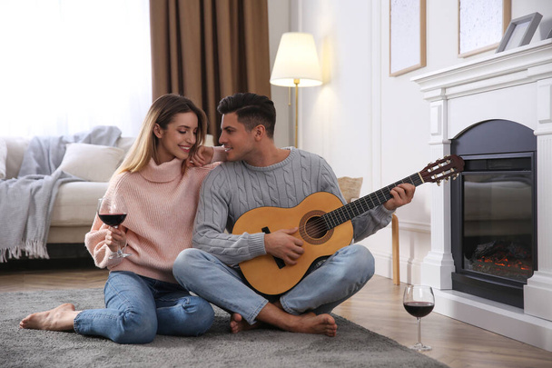 Happy couple spending time together near fireplace at home - Φωτογραφία, εικόνα