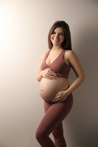 Pregnant young woman touching belly on beige background - Fotó, kép