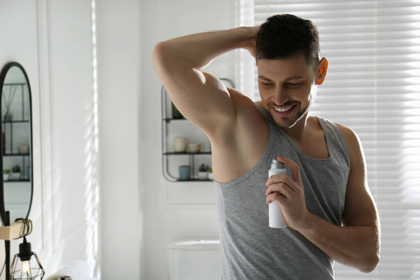 Handsome man applying deodorant in bathroom. Space for text - Foto, Imagen