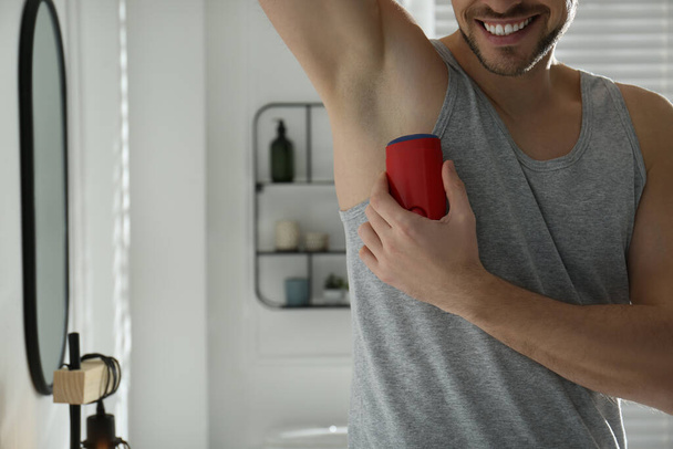 Man applying deodorant in bathroom, closeup. Space for text - Foto, afbeelding