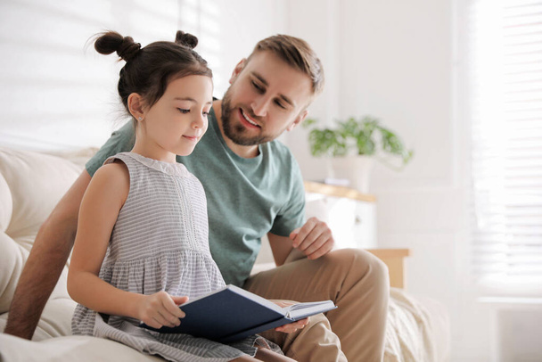 Little girl with father reading fairy tale in living room - Foto, imagen