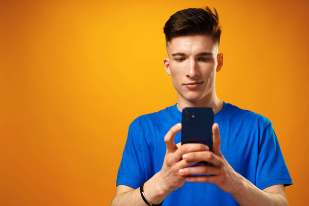 Young man using smartphone against yellow background - Фото, изображение