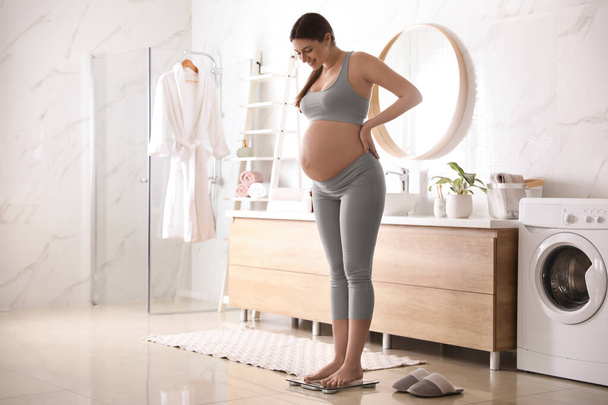 Pregnant woman standing on scales in bathroom - Foto, Bild