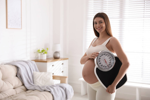 Young pregnant woman with scales at home. Space for text - Фото, изображение