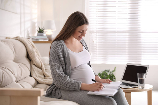 Pregnant woman working on sofa at home. Maternity leave - Foto, afbeelding