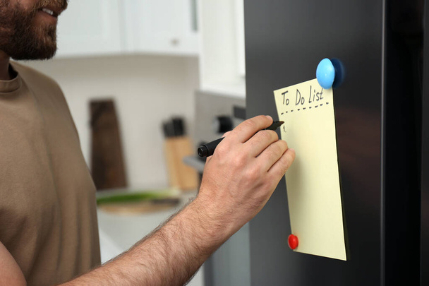 Man writing to do list on refrigerator door in kitchen, closeup - 写真・画像