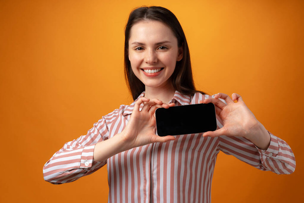 Happy smiling young woman showing you black smartphone screen with copy space - Foto, Imagem