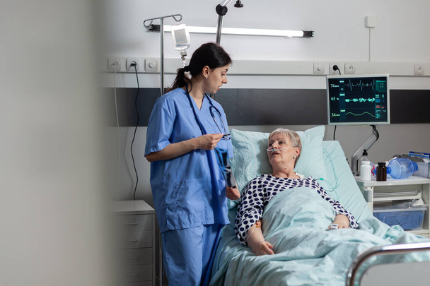 Νοσοκόμα συζητά με ηλικιωμένους ασθενείς κατά την επίσκεψη για ακτινογραφία θώρακος - Φωτογραφία, εικόνα