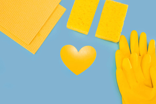 Top view photo of yellow paper heart, rubber gloves, napkins, washcloths, on isolated blue background with blank space - Photo, image