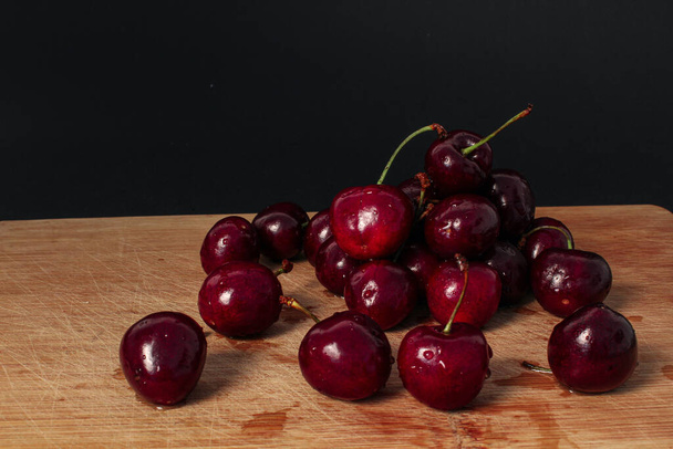 Pile of fresh cherries on wooden desk, black background. - Foto, imagen