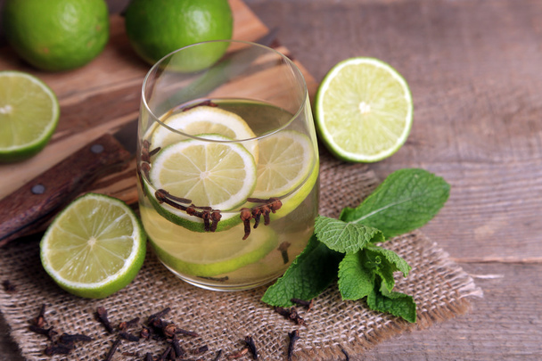 Fresh summer drink with lime and cloves in glass, on color wooden background - Photo, image