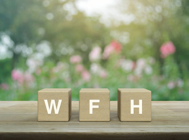 WFH letter on block cubes on wooden table over blur pink flower and tree in garden, Business work from home concept - Foto, Imagem