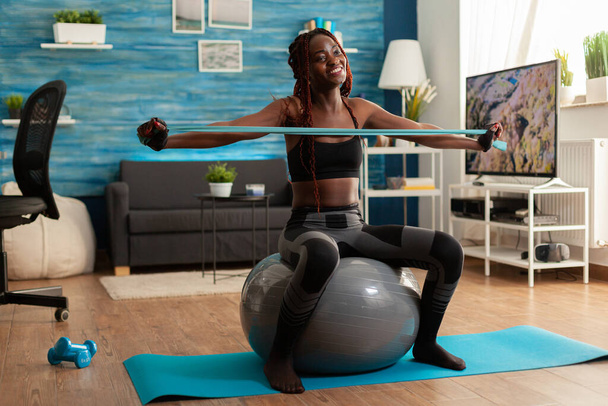 Coupe athlétique joyeuse femme noire travaillant sur le muscle arrière avec bande de caoutchouc - Photo, image