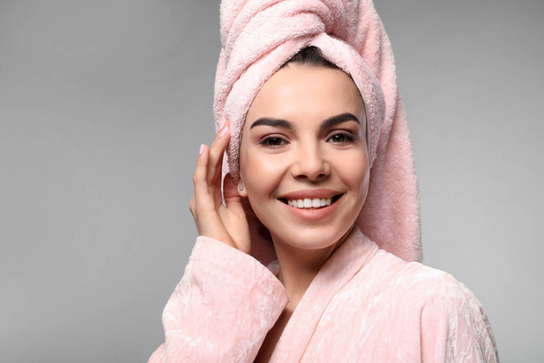 Happy young woman in bathrobe with towel on head against light grey background. Washing hair - Фото, изображение