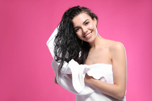 Happy young woman drying hair with towel after washing on pink background - Fotó, kép