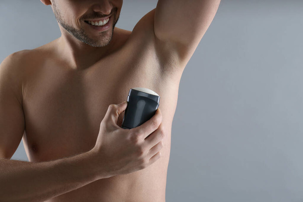 Man applying deodorant on grey background, closeup. Space for text - Фото, изображение
