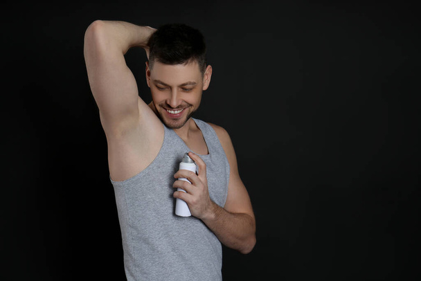 Handsome man applying deodorant on black background. Space for text - Fotografie, Obrázek