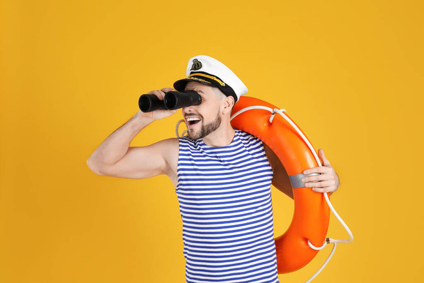Sailor with orange ring buoy looking through binoculars on yellow background - Fotoğraf, Görsel