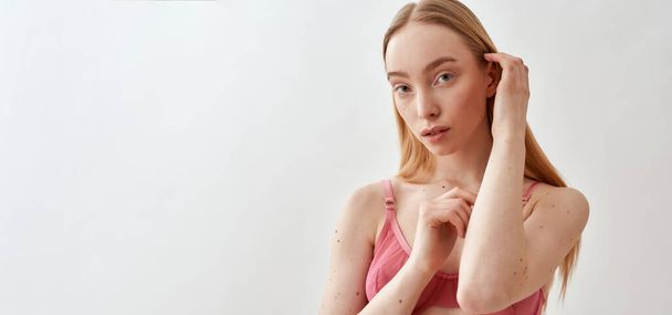 Portrait of sensual young caucasian female model wearing pink transparent bra looking at camera, adjusting her hair while posing isolated over light gray background - Fotó, kép