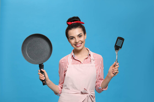 Housewife with frying pan and spatula on light blue background - Fotografie, Obrázek