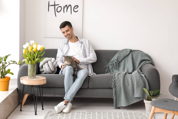 Young man with cute cat in living room - Photo, Image