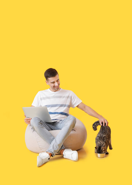 Молодий чоловік з милою кішкою використовує ноутбук на кольоровому фоні
 - Фото, зображення
