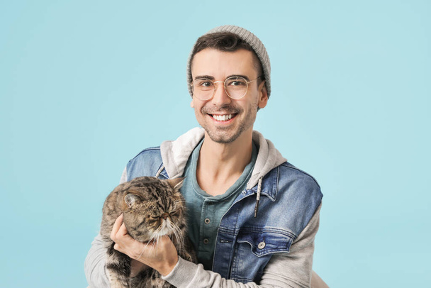 Young man with cute cat on color background - Photo, Image