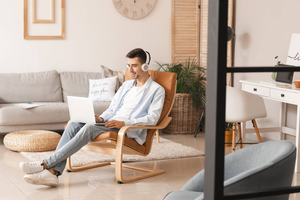 Fiatal férfi fülhallgatóban, laptoppal otthon - Fotó, kép