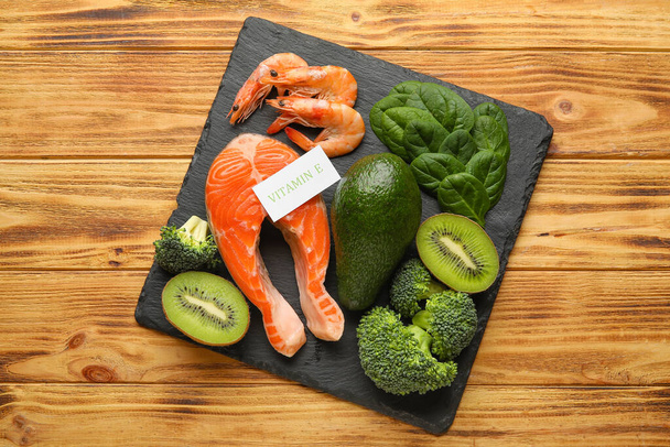Placa de pizarra con productos saludables ricos en vitamina E sobre fondo de madera - Foto, imagen