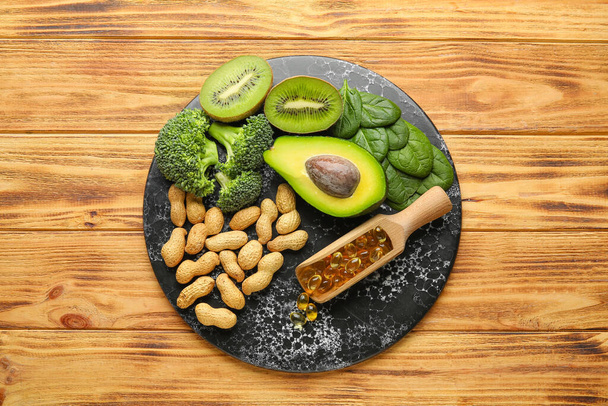 Assiette d'ardoise avec des produits sains riches en vitamine E et capsules d'huile de poisson sur fond en bois - Photo, image