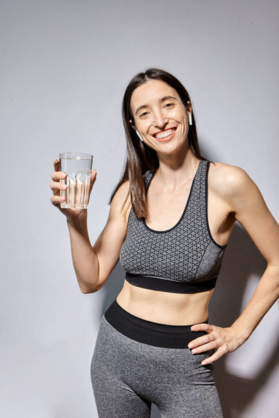 Nainen urheiluvaatteissa ja langattomissa kuulokkeissa juo vettä. terveellisten elämäntapojen ja liikunnan käsite - Valokuva, kuva