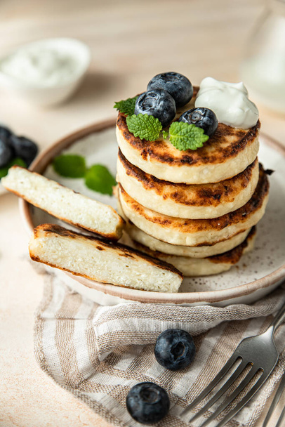 Fried cottage cheese pancakes or fritters with blueberry and sour cream on a plate. Gluten free. Traditional breakfast of Ukrainian and Russian cuisine. - 写真・画像